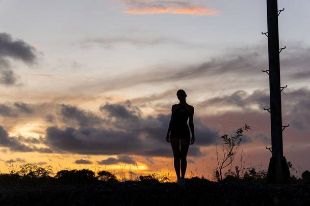 Die Silhouette einer Frau steht kraftvoll vor dem Hintergrund eines farbenfrohen Sonnenuntergangs und vermittelt Kraft und Ruhe - Foto, Bild