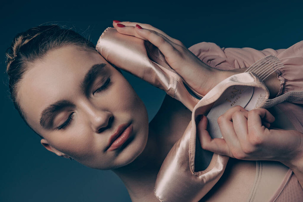 Portrait of young ballerina with closed eyes holding pointe shoes in her hands. Graceful beautiful ballerina. Ballet art, grace, flexibility, motion. - Photo, Image