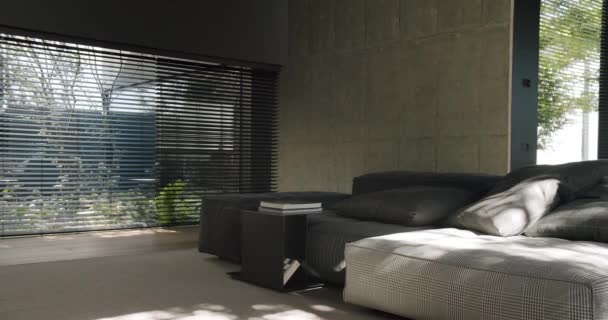 Современная спальня с большой кроватью, бетонными стенами и солнечным светом, проникающим через оконные жалюзи. Современная гостиная с бетонными стенами и стильными жалюзи - Кадры, видео