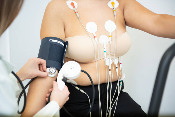 A healthcare professional administers a cardiology test with electrodes and blood pressure cuff. - Photo, Image