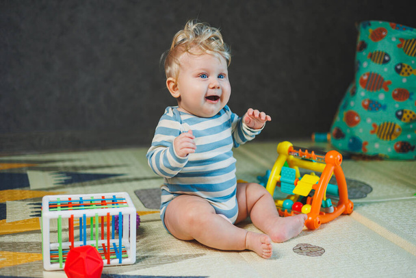Zdjęcie siedmiomiesięcznego chłopca siedzącego na podłodze i bawiącego się zabawkami. Dziecko uśmiecha się i bawi zabawkami.. - Zdjęcie, obraz