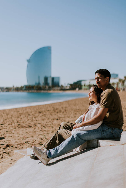 Pari rentoutuu Barcelonassa hiekkarannalla, jossa ikoninen hotelli taustalla - Valokuva, kuva