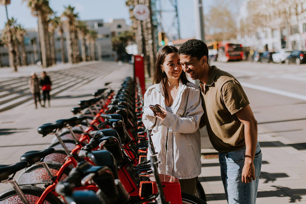 Nuori pari nauttii tuulinen päivä valita polkupyöriä vuokra-asemalta Barcelonassa. - Valokuva, kuva