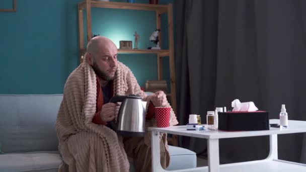 Homem doente preparando e bebendo chá quente sentado no sofá em casa. Conceito de saúde, doença e pessoas. - Filmagem, Vídeo