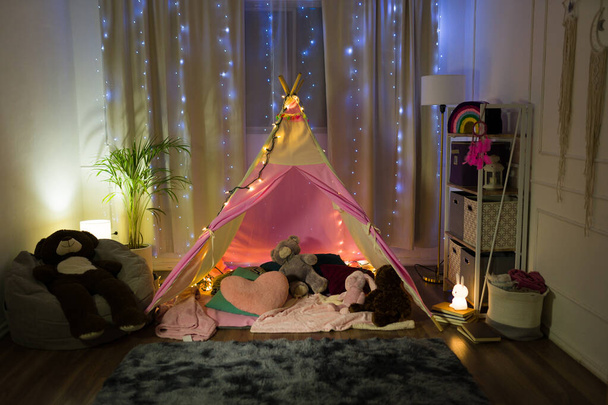 Encantador cambio de imagen dormitorio crea un caprichoso campamento nocturno para una niña, completo con luces de hadas y juguetes de peluche - Foto, imagen