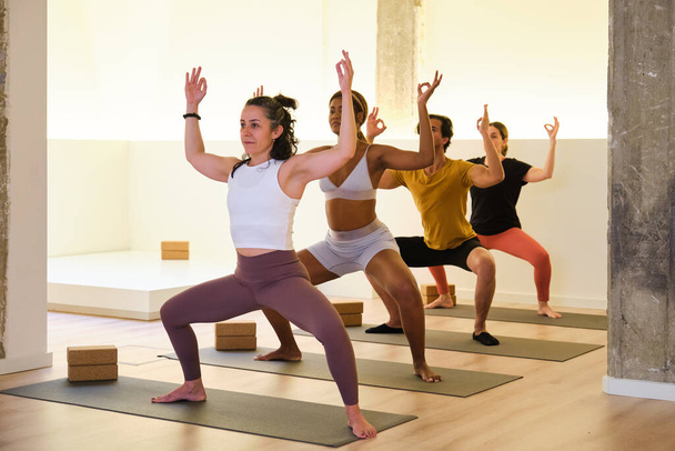 Un gruppo di persone praticano yoga, Utkata Konasana o dea, in una stanza. La scena è calma e pacifica, poiché le donne si concentrano sulle loro pose e respirano. - Foto, immagini
