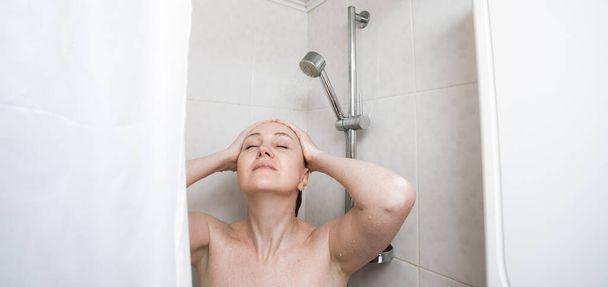Szczupła kobieta stoi w łazience i myje długie blond włosy pod prysznicem. Obraz na temat zdrowia, higieny i pielęgnacji włosów. - Zdjęcie, obraz