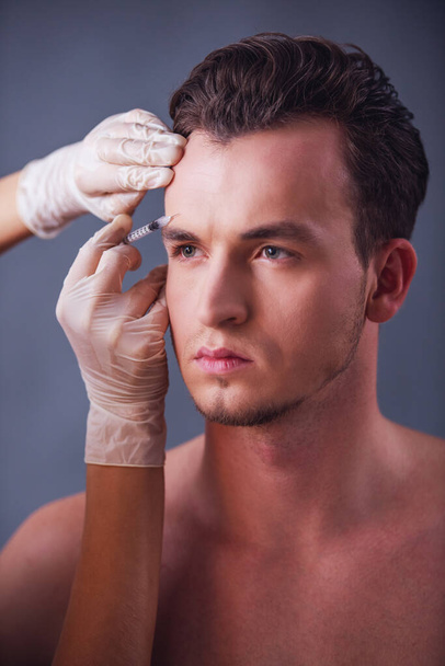 Knappe jongeman krijgt gezicht injectie, op grijze achtergrond - Foto, afbeelding