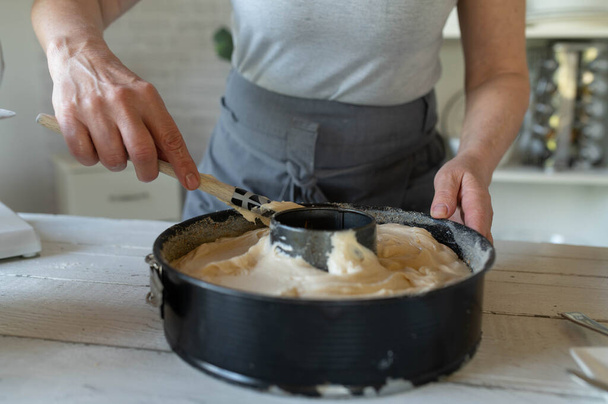 Разглаживание теста или теста в кастрюле для выпечки женскими руками. Готовлю торт на кухне. - Фото, изображение