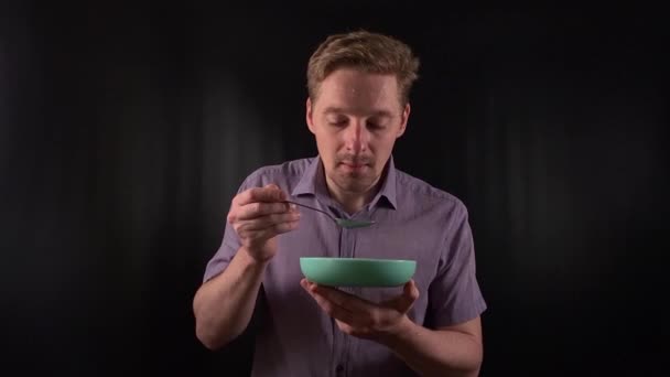 Captivating portrait of a stylish young man with stubble, donning a vibrant purple shirt on a sleek black backdrop, takes bites of meal, exuding an effortless cool vibe. Lifestyle, fashion or culinary - Footage, Video