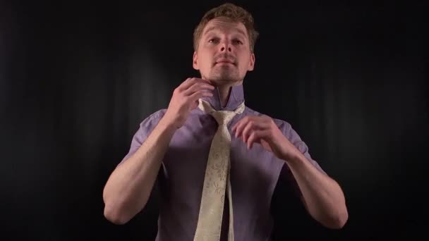 Dapper portrait of a stylish young man adjusting a crisp white necktie. Clad in a vibrant purple shirt with casual stubble he exudes an effortlessly cool yet refined vibe on the minimal black backdrop - Footage, Video