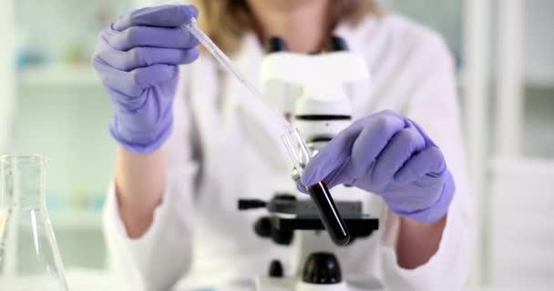 Επιστήμονας στάζει νερό σε γυάλινο δοκιμαστικό σωλήνα με μαύρο αργό πετρέλαιο. Γυναίκα με ελαστικά γάντια προετοιμάζει την ουσία για εξέταση στο μικροσκόπιο στο εργαστήριο - Πλάνα, βίντεο