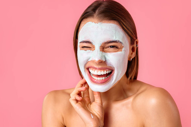 Beautiful happy woman using cleansing clay face mask for blackheads and enlarged pores isolated on pink background. Skin care, cosmetology, beauty concept. - Photo, Image