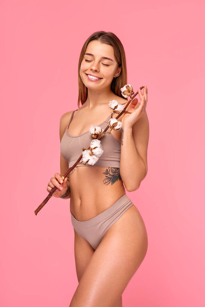 Bella donna in lingerie tenuta ramo di cotone isolato su sfondo rosa. Cura della pelle del corpo, cosmetologia, concetto di bellezza. - Foto, immagini