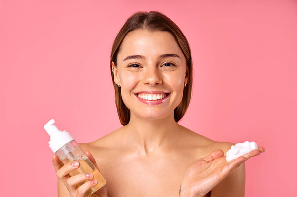 Mulher bonita limpando seu rosto com espuma isolada no fundo rosa. Cuidados com a pele facial, cosmetologia, conceito de beleza. - Foto, Imagem