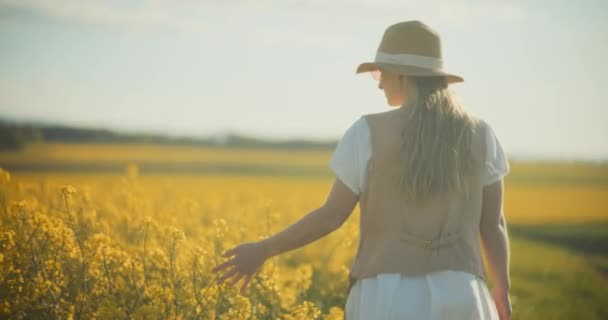Ein fesselndes Porträt einer Frau, die anmutig inmitten eines lebendigen Rapsfeldes spaziert und Gefühle der Gelassenheit und Verbundenheit mit der Natur hervorruft - Filmmaterial, Video