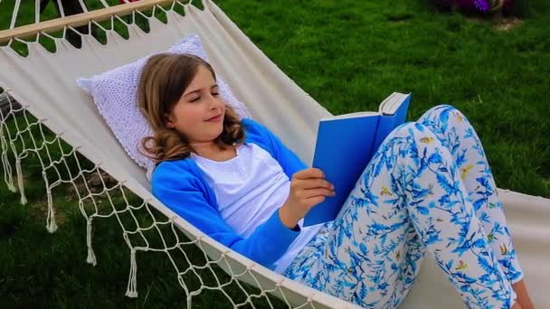 Tyttö lukee kirjaa riippumatossa puutarhassa
 - Materiaali, video