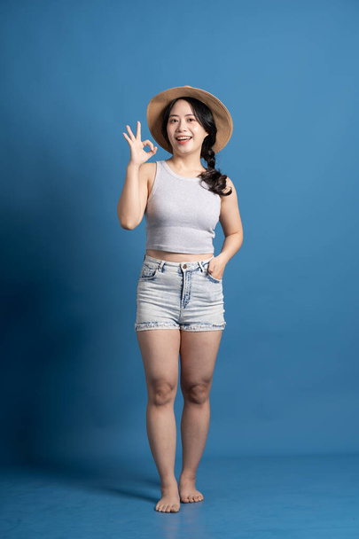 Портрет азиатской девушки, позирующей на синем фоне, путешествующей летом - Фото, изображение