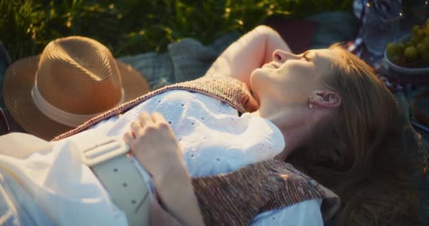 Capture a essência do lazer como uma mulher sorridente se entrega ao relaxamento em um cobertor de piquenique aconchegante em meio à beleza naturezas - Filmagem, Vídeo