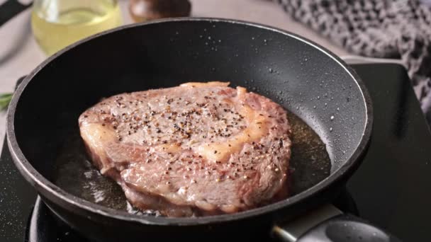 Kuchař uvaří hovězí steak na pánvi v kuchyni a otočí ho na druhou stranu, zblízka. Proces vaření lahodného steaku. - Záběry, video