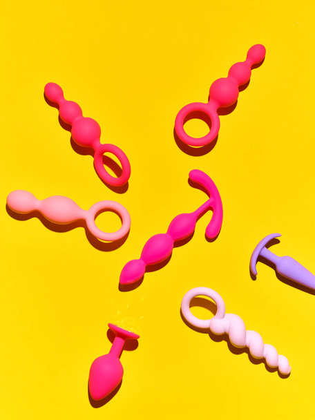 Bright sex toys background. anal plugs and dildo over yellow paper backdrop - Foto, afbeelding