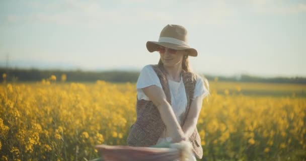Ein fesselndes Porträt einer Frau, die anmutig inmitten eines lebendigen Rapsfeldes spaziert und Gefühle der Gelassenheit und Verbundenheit mit der Natur hervorruft - Filmmaterial, Video