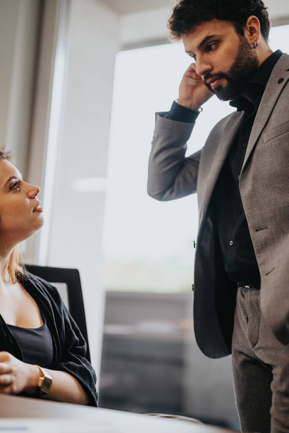 Μια επαγγελματική συζήτηση κλιμακώνεται καθώς ένας άνδρας εργάτης εκφράζει ανησυχία ενώ μια γυναίκα συνάδελφος ακούει προσεκτικά σε ένα καλά φωτισμένο περιβάλλον γραφείου.. - Φωτογραφία, εικόνα