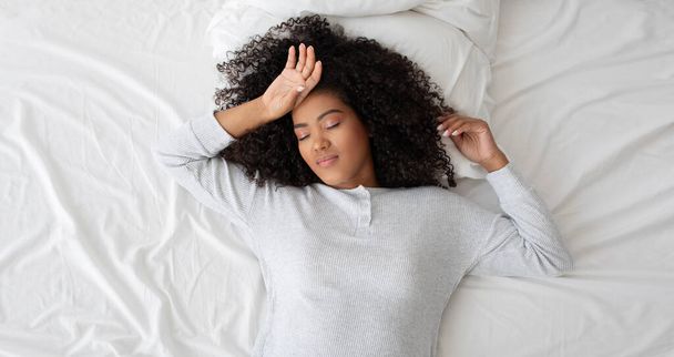 Spanyol nő fekszik az ágyon, kezeit a fejére helyezve. A jelenet rögzíti a pihenés vagy elmélkedés pillanatát, felülnézetből - Fotó, kép