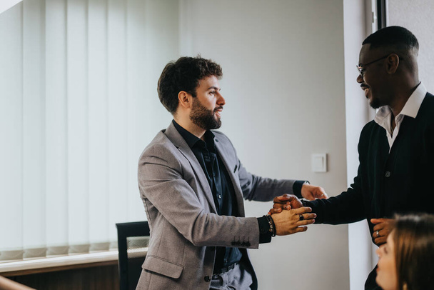 Een openhartig moment in een helder kantoor als twee mannelijke professionals, verschillend in etniciteit, vieren een succesvolle ontmoeting met een handdruk, signalering samenwerking en teamwork. - Foto, afbeelding