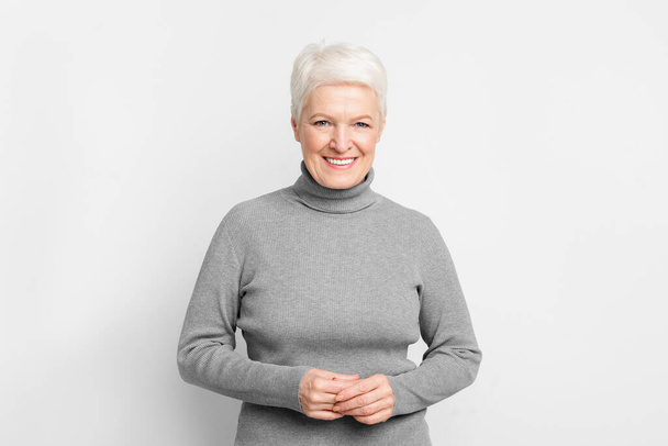 Allegro anziana donna europea con le mani strette, illustrando s3niorlife appagamento su sfondo grigio - Foto, immagini