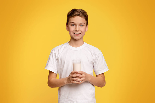 Tejimádó. Vidám tinédzser fiú mosolygós üveg friss tej, narancs háttér - Fotó, kép