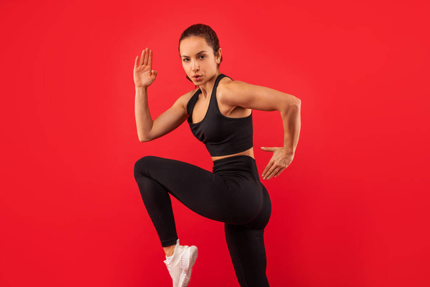 Egy nő fekete sportmelltartó felsőben és egyforma lábszárvédőben, bemutatva a sportos testalkatát. Magabiztosan áll, edzésre vagy edzésre készen.. - Fotó, kép