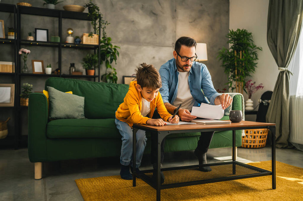 Père avec des lunettes et fils faire des devoirs et apprendre ensemble à la maison - Photo, image