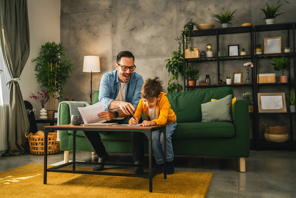 Père avec des lunettes et fils faire des devoirs et apprendre ensemble à la maison - Photo, image