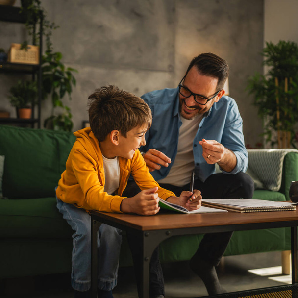 Vater mit Brille und Sohn machen Hausaufgaben und lernen gemeinsam zu Hause - Foto, Bild