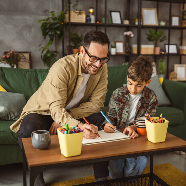 Father with eyeglasses and son caucasian draw and paint together at home leisure activity - Photo, Image