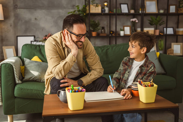 Vater mit Brille und Sohn zeichnen und malen gemeinsam zu Hause Freizeitaktivität - Foto, Bild