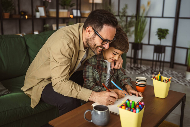 Vater mit Brille und Sohn zeichnen und malen gemeinsam zu Hause Freizeitaktivität - Foto, Bild