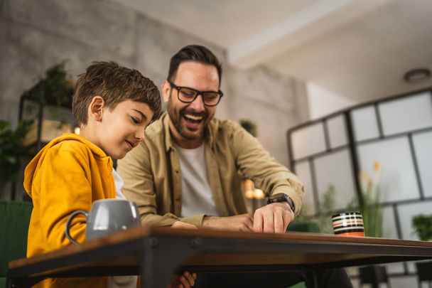 Padre con occhiali e figlio caucasico gioco da tavolo insieme a casa felice godere - Foto, immagini