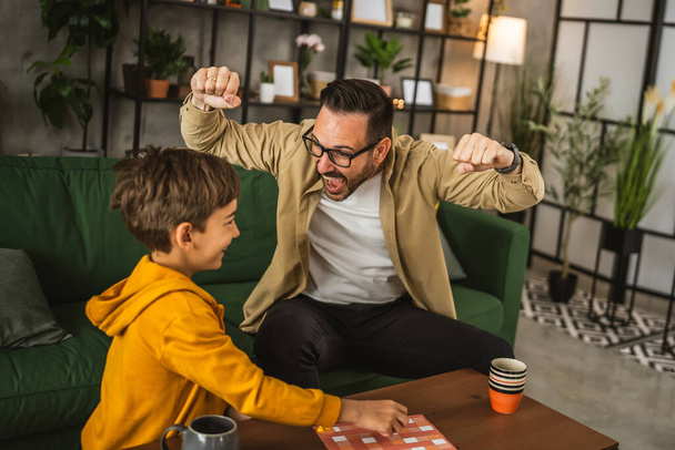 Father with eyeglasses and son caucasian play board game together at home happy enjoy - Photo, Image