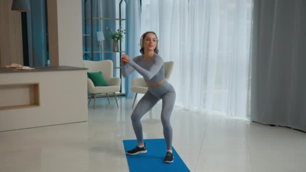 Boldog sportos nő guggolás edzés a nappaliban női torna fenék testmozgás sport otthon fogyás kaukázusi lány fitness edző sportnő zenét hallgatni a fejhallgató edzés motiváció - Felvétel, videó