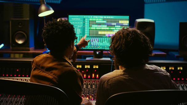 Joukkue ääniteknikot työskentelevät tallennus ja editointi kappaleita ammatillinen studio valvomossa, yhteistyötä mix ja master äänitiedostoja. Muusikko ja teknikko painavat liukusäätimiä. Kamera B. - Valokuva, kuva