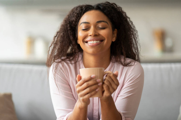 Obraz ten rejestruje spokojny Afryki amerykańskiej pani korzystających ciepły napój w domu, ucieleśniając relaks i komfort - Zdjęcie, obraz