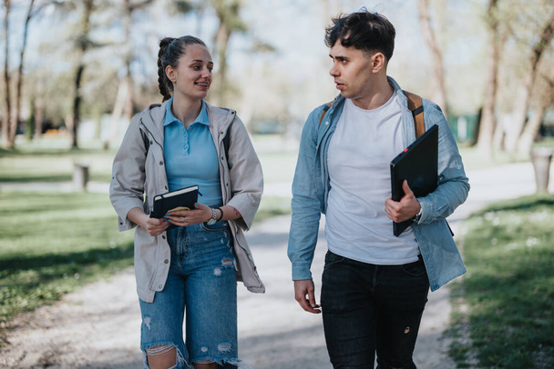 Dwóch studentów korzystających z przyjaznej rozmowy podczas spaceru z książkami w spokojnej okolicy parku. - Zdjęcie, obraz