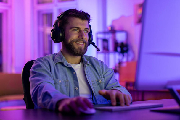 Ein Millennial-Typ setzt zu Hause ein Gaming-Headset auf, sein ruhiger Gesichtsausdruck vermittelt die heitere Spielsucht in einem personalisierten Raum - Foto, Bild