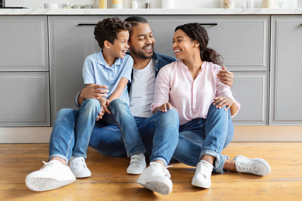 Laughing African American family sitting on the kitchen floor, depicting a light-hearted and engaging moment - Photo, Image