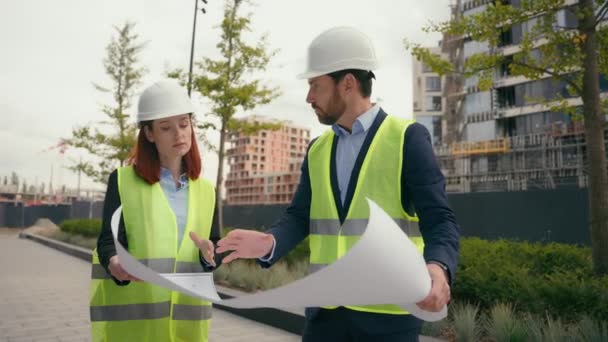 Két vállalkozó építőmérnökök megvitatni elektromos karbantartás tervrajzot papír partnerség megvitatása csapatmunka városi épületek projekt építők nő férfi építészek terv városfejlesztés - Felvétel, videó