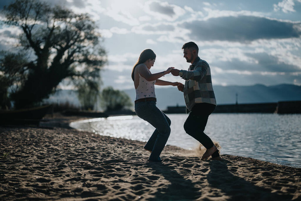 Ένα ευτυχισμένο ζευγάρι απολαμβάνει έναν ανέμελο χορό σε μια αμμώδη παραλία κατά τη διάρκεια των διακοπών τους, ενσωματώνοντας τη χαρά και τη συντροφικότητα σε ένα όμορφο φυσικό σκηνικό. - Φωτογραφία, εικόνα