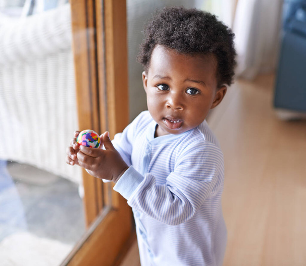 Μωρό, πορτρέτο και μπάλα παίζει στο σπίτι για την ανάπτυξη στο διαμέρισμα για παιχνίδια, ευεξία ή παιδική ηλικία. Μαύρος, παιδί και πρόσωπο στο παράθυρο του σπιτιού στην Κένυα σε μικρό αγόρι, διασκέδαση, φυτώριο ή υγεία. - Φωτογραφία, εικόνα