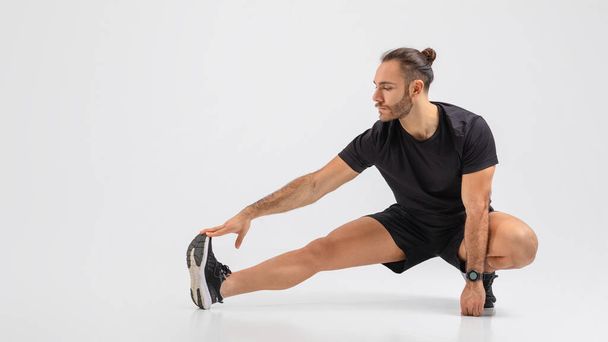 Un uomo in camicia nera e pantaloncini è impegnato in un esercizio di stretching all'aperto. Sta allungando braccia, gambe e schiena per migliorare la flessibilità e prevenire lesioni. - Foto, immagini